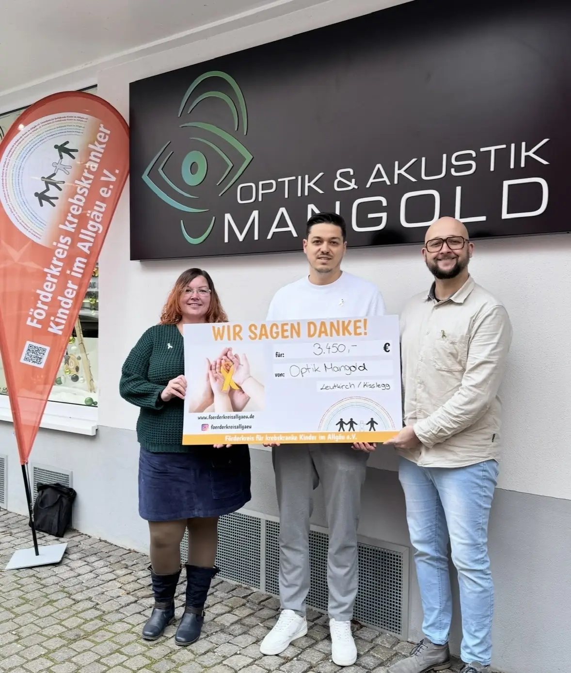 Übergabe des Spendenschecks über 3.450 Euro an den Förderkreis krebskranker Kinder im Allgäu e. V. vor dem Geschäft von Optik & Akustik Mangold